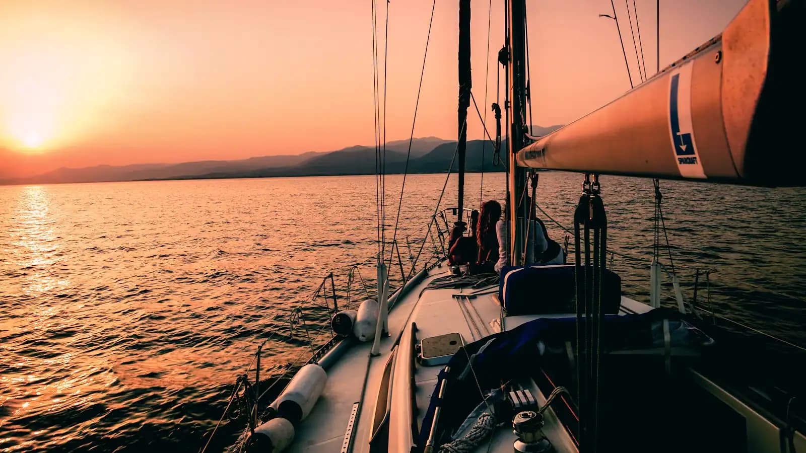 A sailing boat silhouetted on calm water as the sun drops toward the horizon